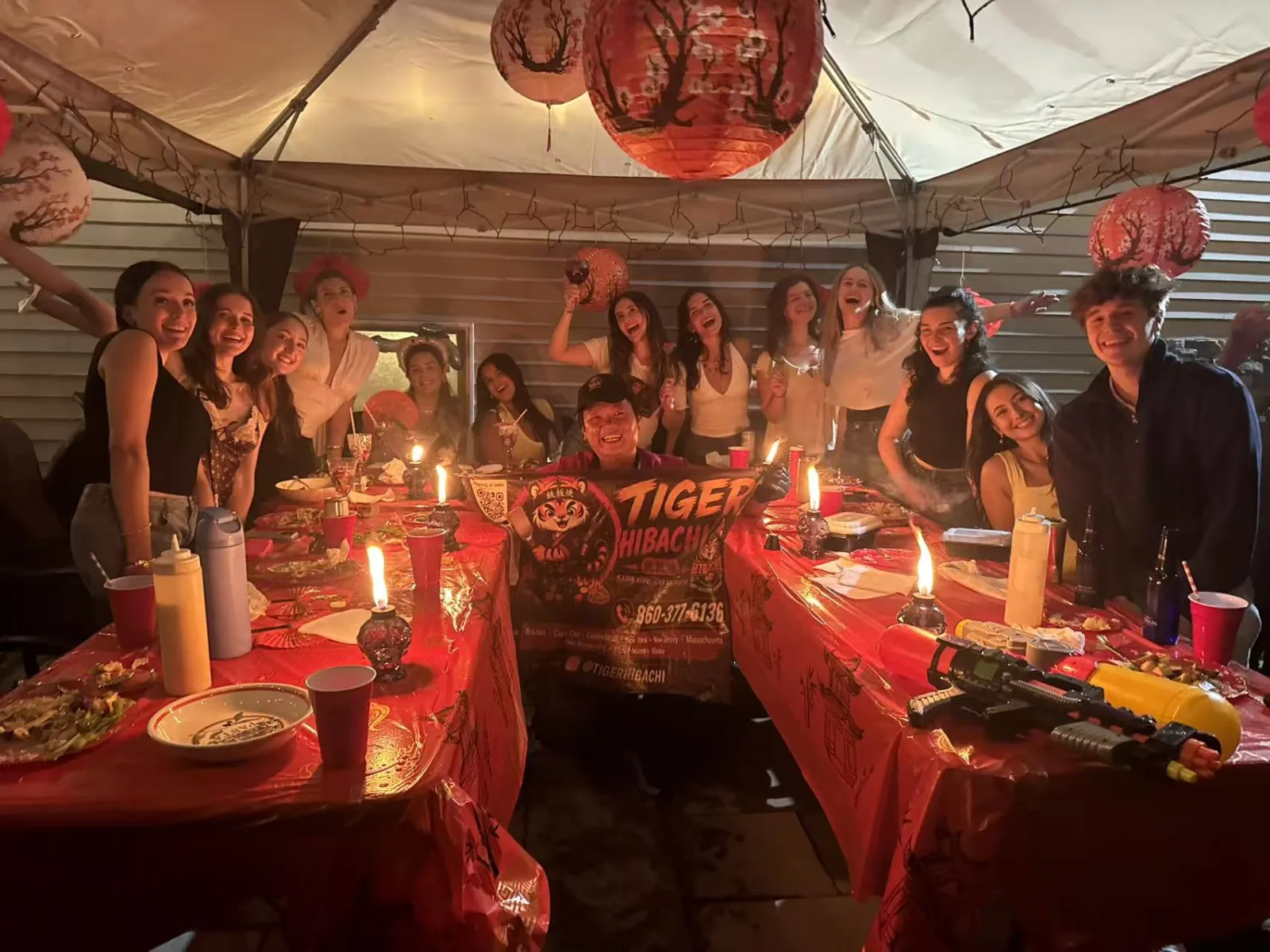 Group of friends laughing together under red paper lanterns at a nighttime Tiger Hibachi party in Rhode Island