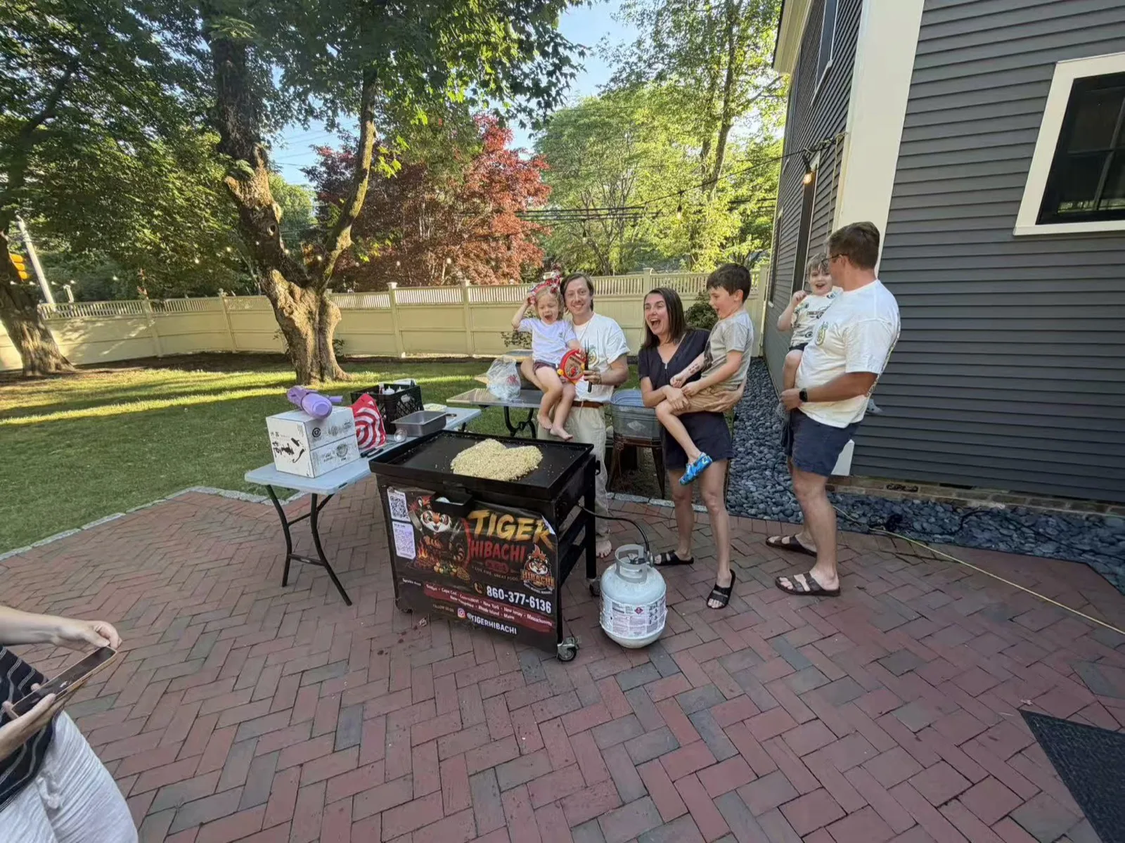 Group of friends posing beside the Tiger Hibachi grill cart on a patio in Rhode Island
