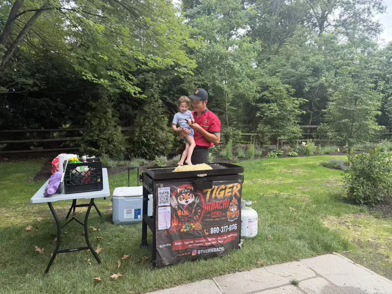 Tiger Hibachi chef holding a young child beside the grill cart in a Rhode Island garden