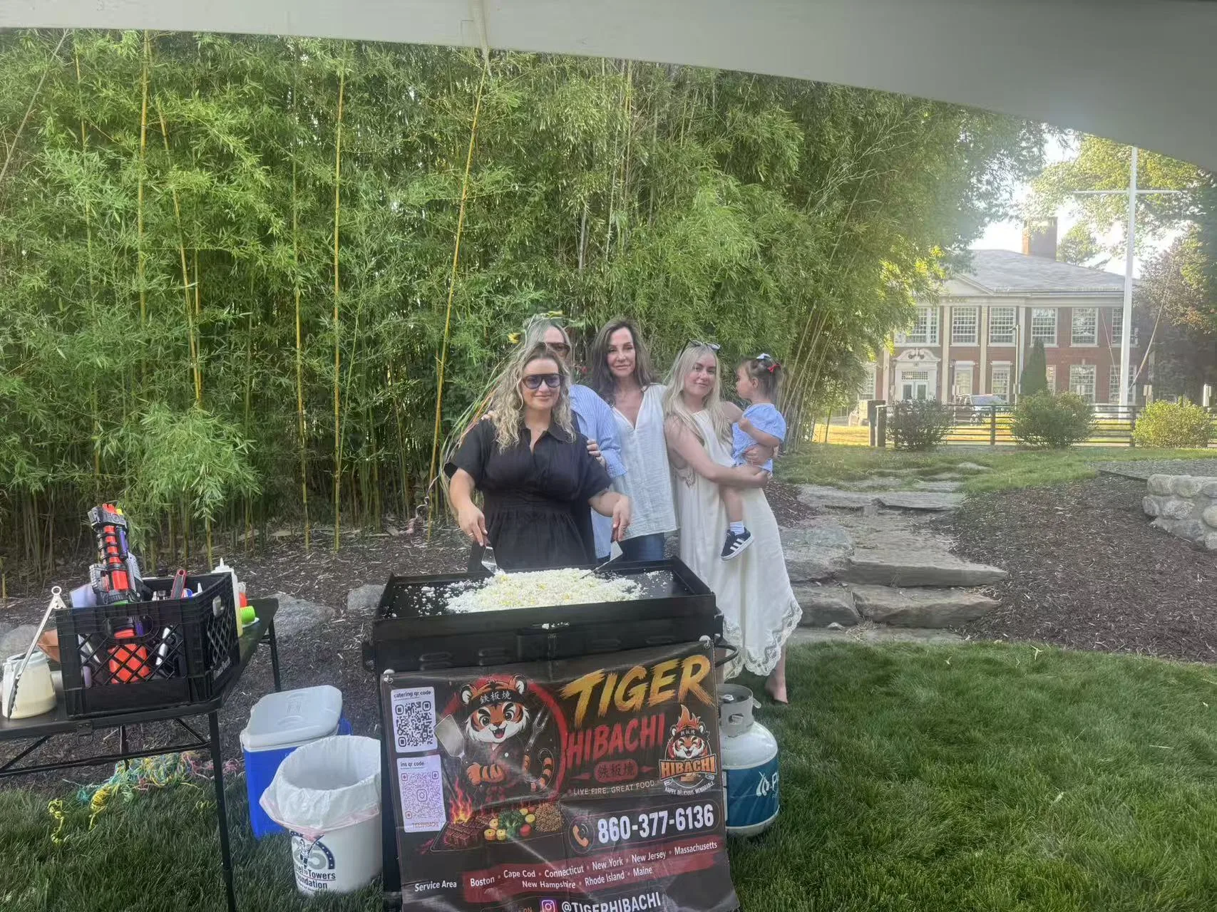 Friends posing together behind the teppanyaki griddle while fried rice cooks at a Tiger Hibachi party in Rhode Island