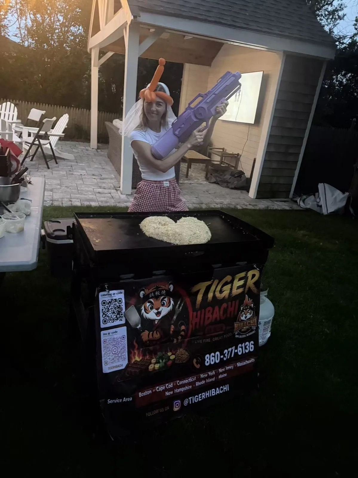 Tiger Hibachi chef holding a large toy prop beside the grill cart at a Rhode Island party