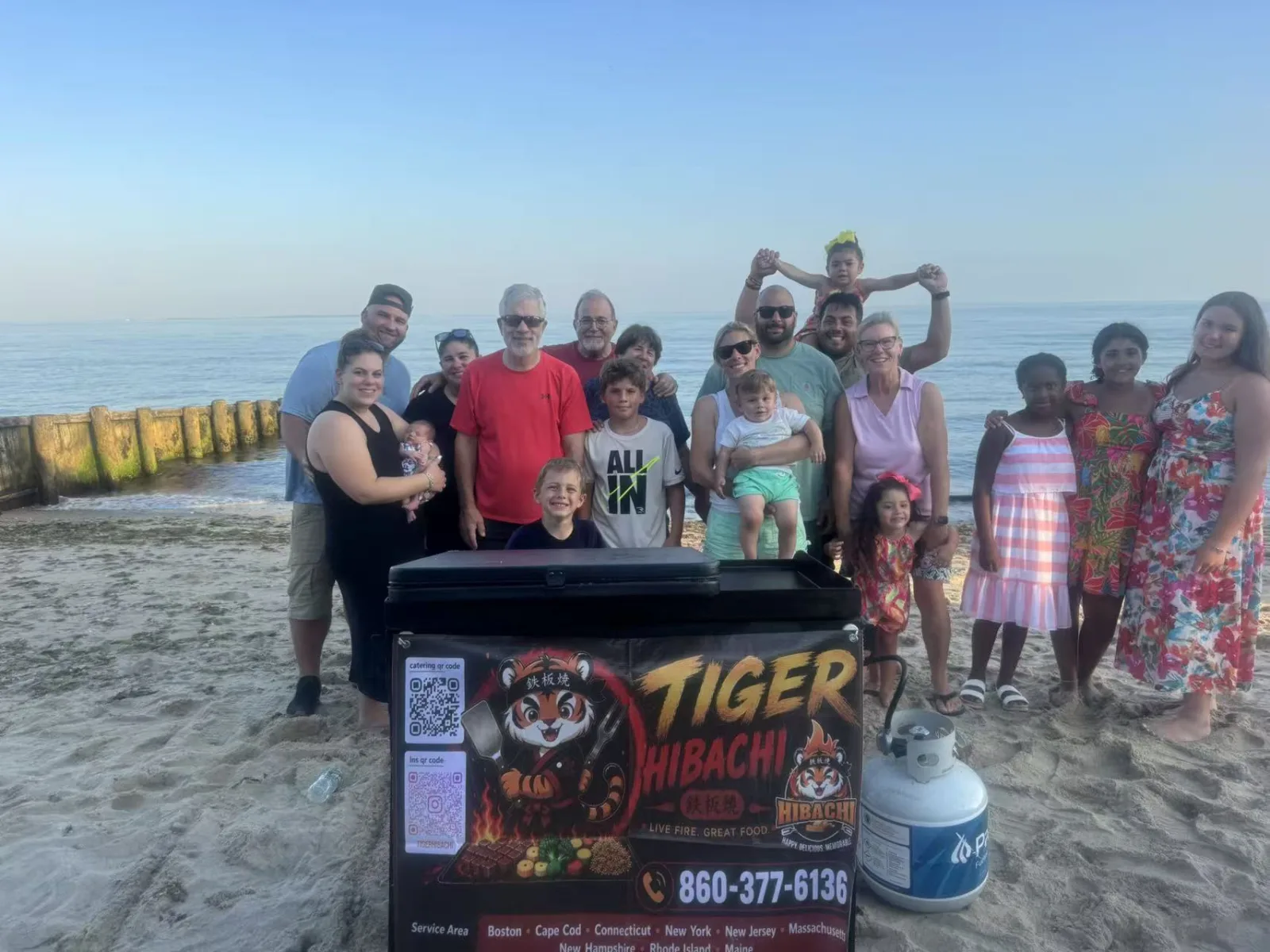 Tiger Hibachi cart set up on the beach with the host family posing together at sunset in Rhode Island