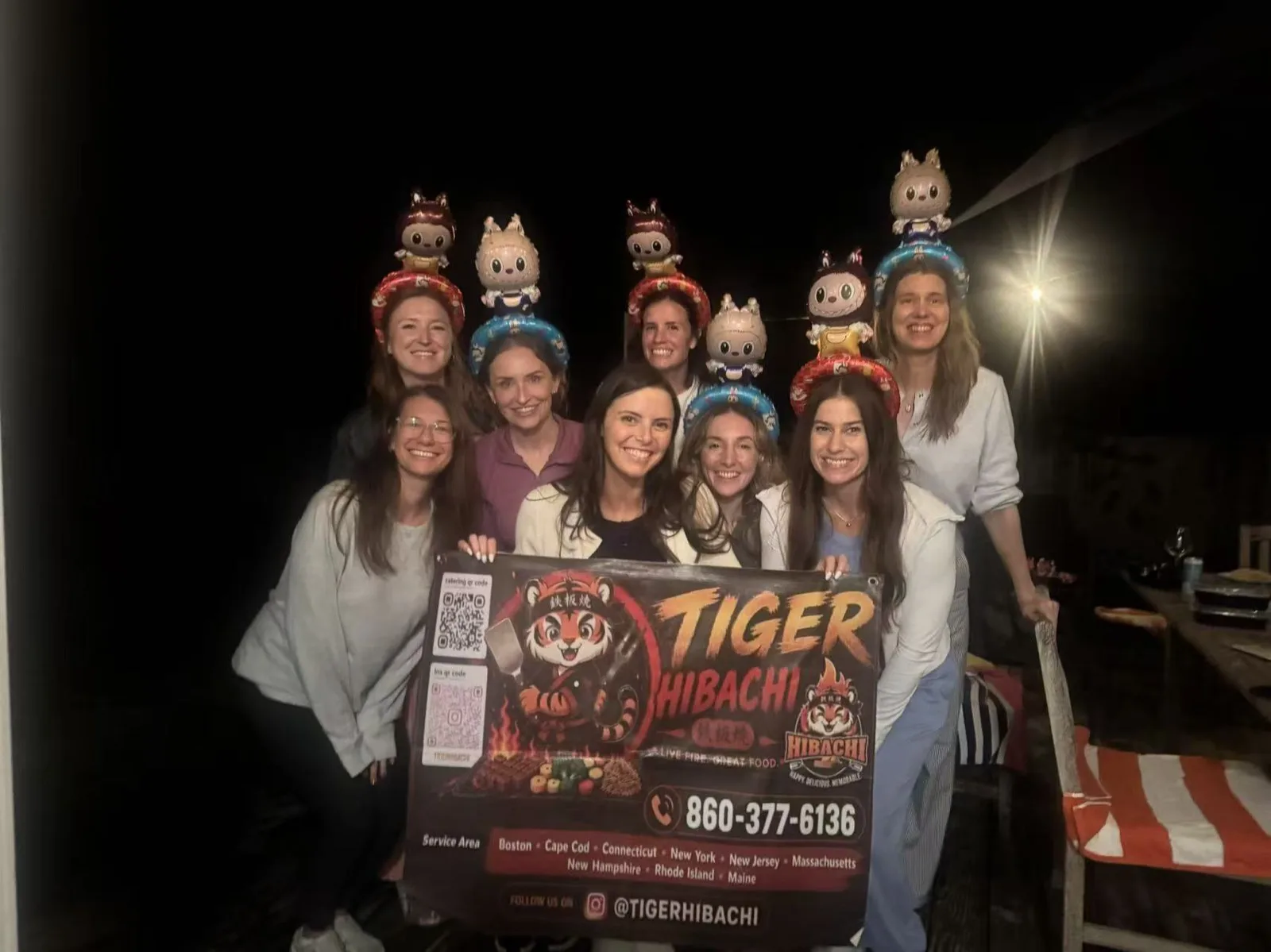 Group of women wearing costume headbands posing together at a nighttime hibachi party in Rhode Island