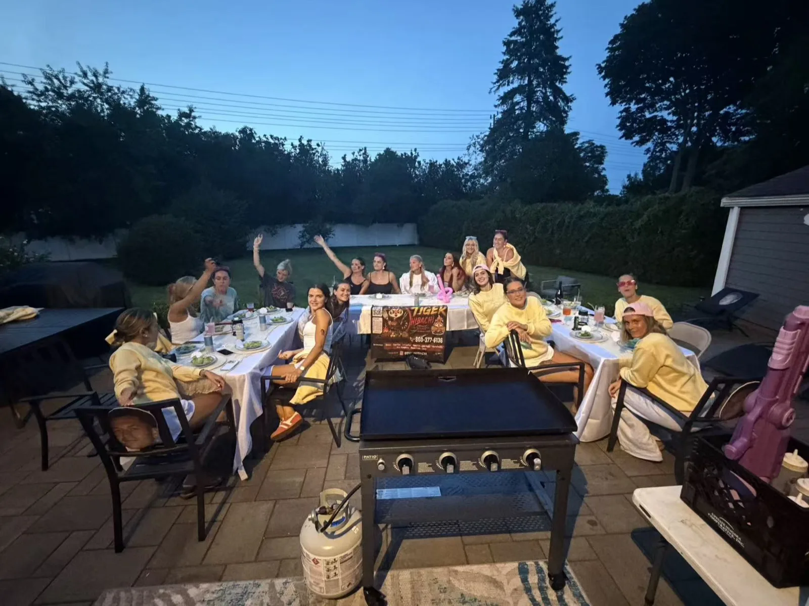 Guests seated at a long table under a pergola for a hibachi party at dusk in Rhode Island