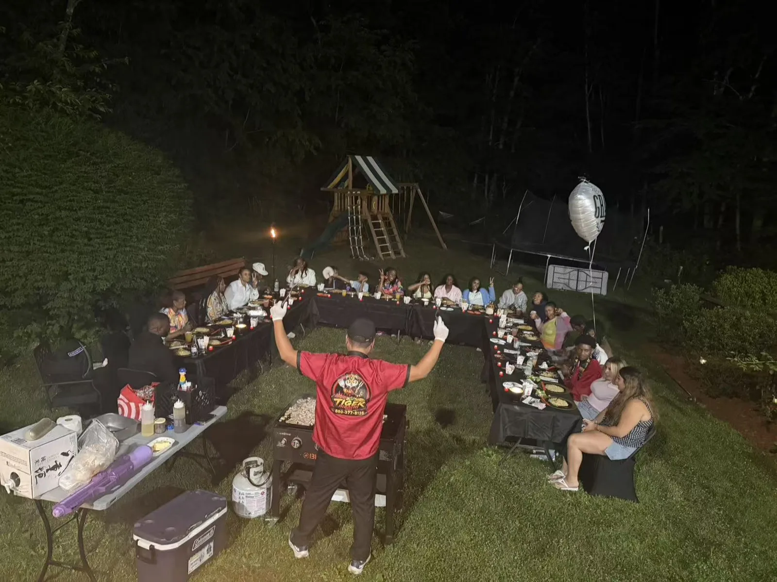 Guests celebrating at a nighttime Tiger Hibachi party with a backyard playground in the background in Rhode Island