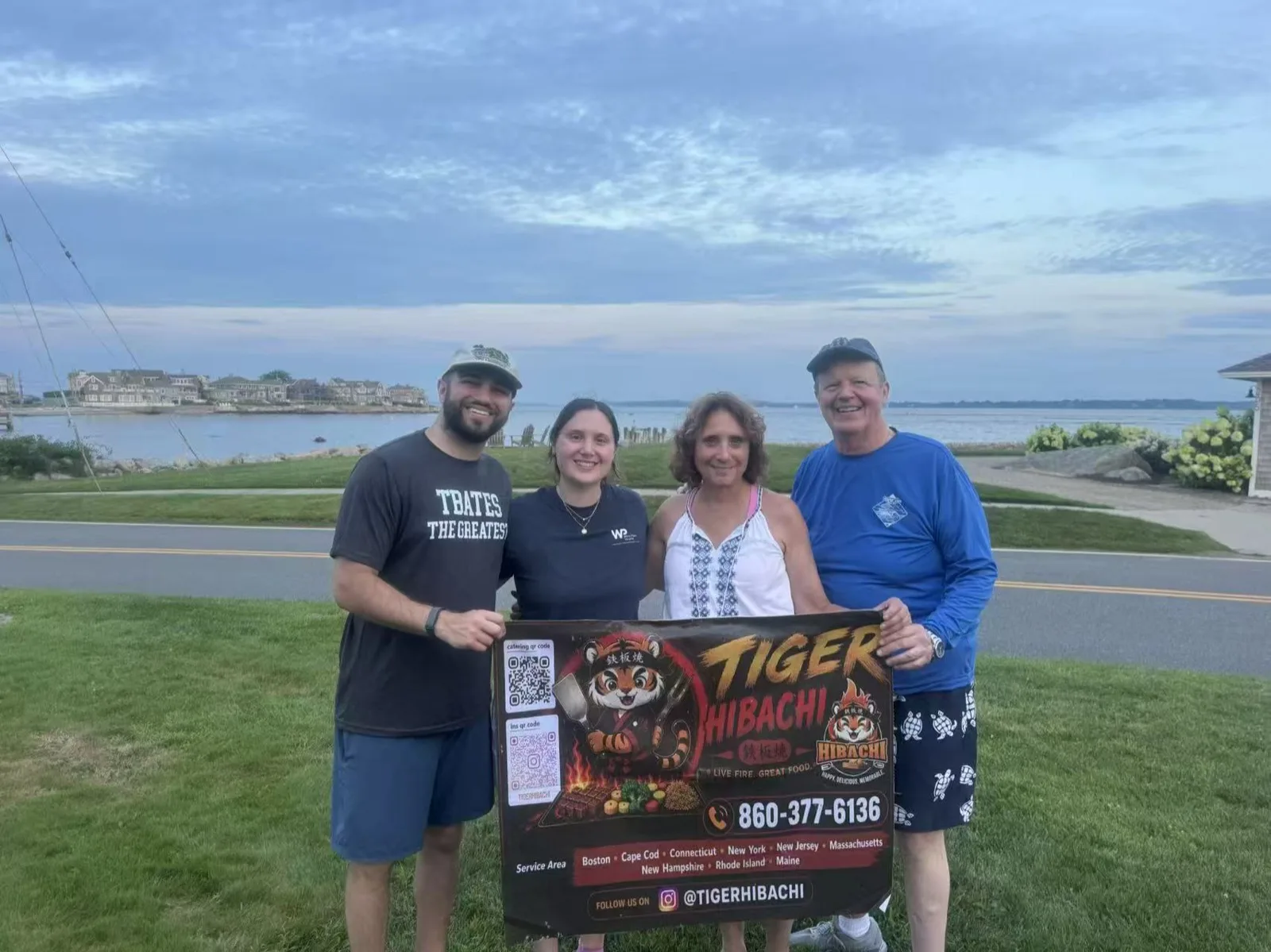 Family posing together with the Tiger Hibachi sign at a waterfront park in Rhode Island